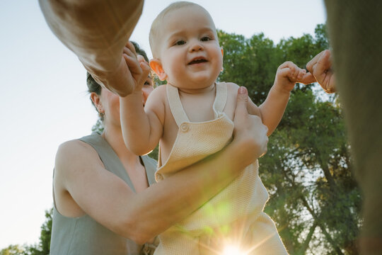 Joyful baby playing outdoors at sunset with family members