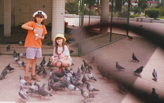 Analog photo of two young girls feeding pigeons in the park &ndash; 1997