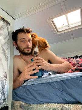 Man Relaxing With Dog in a Camper While Holding a Beverage