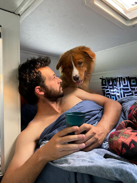Man Relaxing With Dog in a Camper While Holding a Beverage