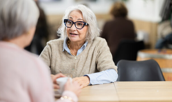 Two mature women having nice conversation at cafe, drinking coffee, friend meeting. Cafe visitors drink coffee, discuss plans, share memories. Casual conversation, friendly atmosphere, coffee break