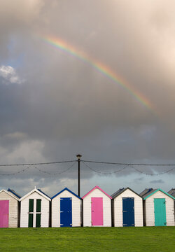 UK, England, Devonshire, Paignton.  A row of colourful  changing huts at the beach, with rainbow overhead.