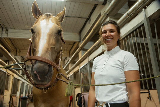 Horsewoman smiling and holding palomino horse in stable