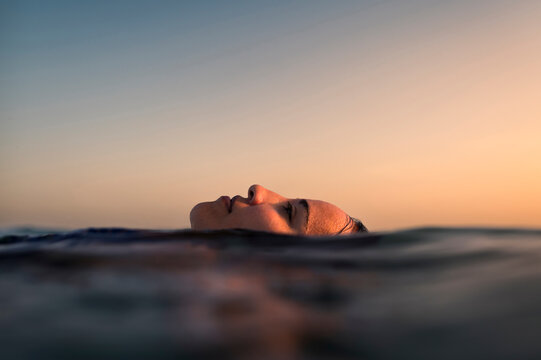 Relaxed woman face floating in the sea at sunset