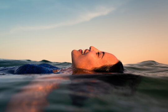 Smiling woman floating in the sea at sunset