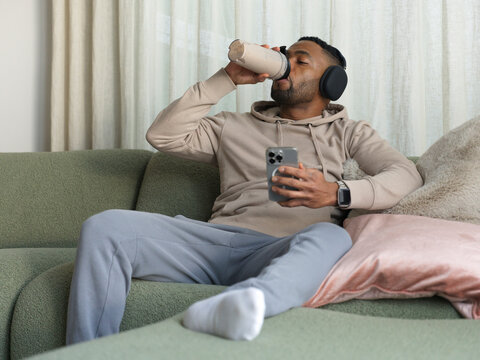 Relaxed Man Enjoying a Protein shake While Using Smartphone at Home