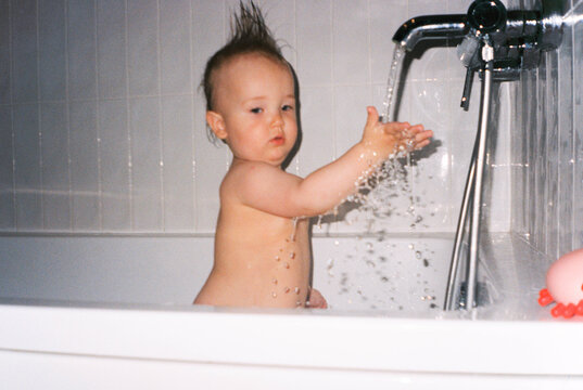 Toddler plays with running water in a bathtub   - film analog