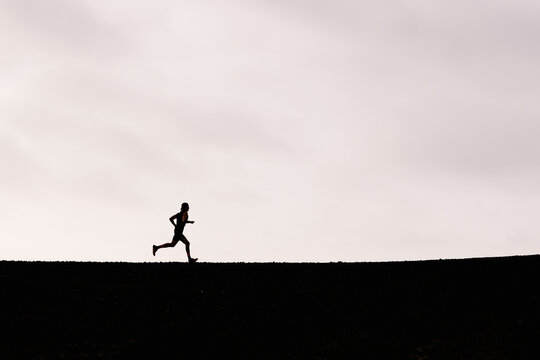 Wide view of the silhouette a runner jogging along a volcanic trail