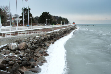 A snow-covered seaside promenade runs along the partially frozen Baltic Sea. Rocks, icy shoreline...