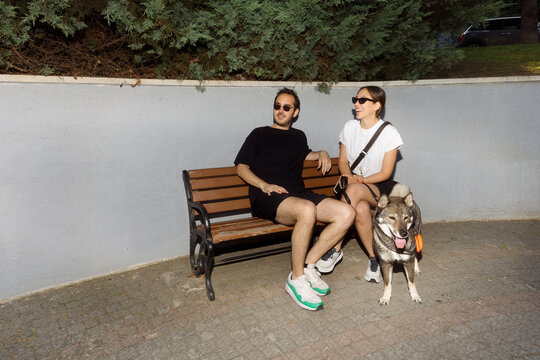 man and young woman sitting in park on bench with dog