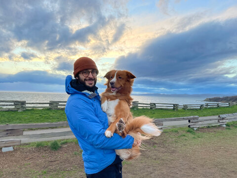 Man Holding Happy Dog at Scenic Beach During Stunning Sunse