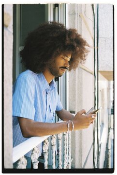 Curly Hair Man Checks Phon on Balcony