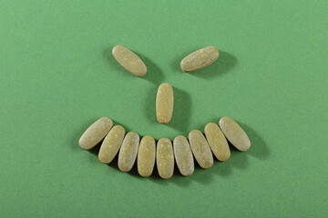 A creative smiley face formed with vitamin pills on a green background, symbolizing health, wellness, and a positive mood