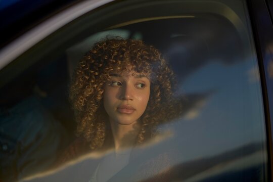 Woman With Curly Hair Gazes Thoughtfully out of a Car Window