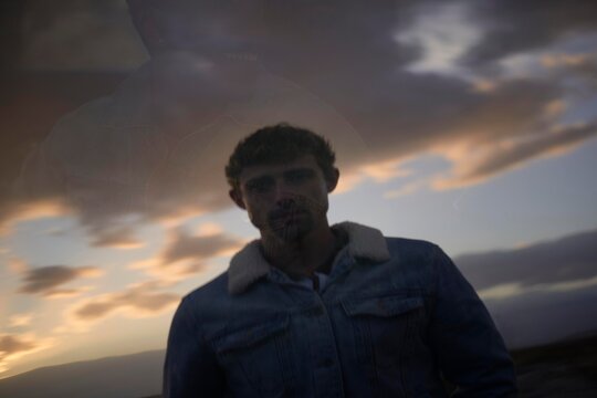 Car Window Reflection of a Man against a Cloudy Sunset Background