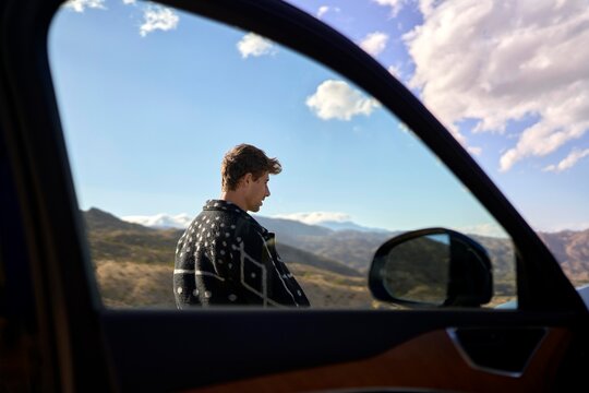Young man enjoying a scenic view next to a car on a sunny day