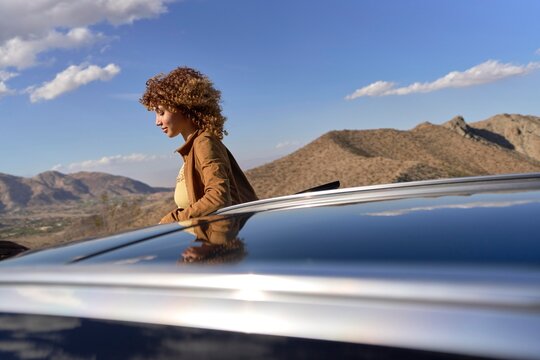 Young Woman Enjoying Scenic Mountain View From Car Roof