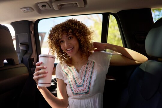 Young Woman Enjoying a Drink Inside a Car on a Sunny Day