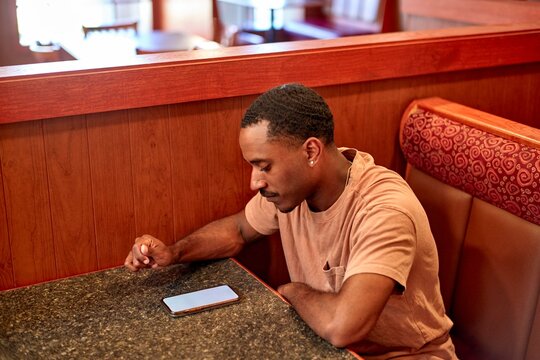 Man Sitting Alone in Restaurant Booth Using Smartphone