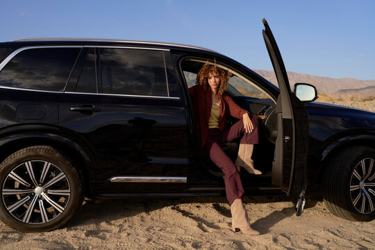 Woman Posing Next to Black SUV in Desert Landscape During Sunset
