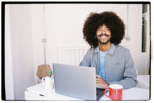Young Man With Curly Hair Working on Laptop in Bright Space