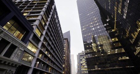 Fototapeta premium golden office lights in glass towers framing commuting corridor, early rush implied, brisk urban energy, layered reflections and towering facades create