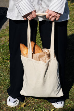 Woman holding a reusable bag filled with fresh baguettes