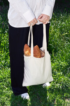 Person holding a reusable bag filled with fresh baguettes