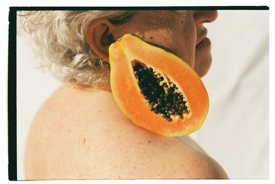 woman with white hair holding a mango on her shoulder 