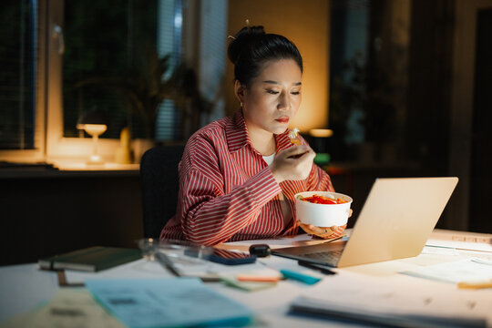 A woman eats while working on a laptop