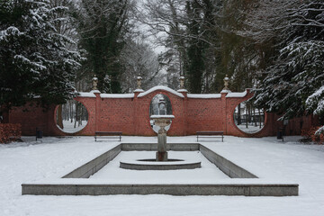 Park dworski w mieście Iłowa w zimowy dzień. Faliste, ażurowe, ceglane ściany, noszące nazwy bram księżycowych wraz ze znajdującymi się w sąsiedztwie nieckami fontann. Ziemię pokrywa śnieg. © boguslavus