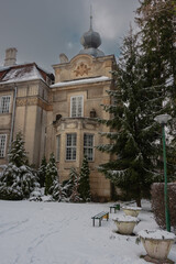 Zabytkowy pałac w parku dworskim w Iłowej, w zachodniej Polsce. Jest zima, dach, gałęzie okolicznych drzew i ziemię pokrywa warstwa śniegu. Niebo jest bezchmurne. © boguslavus