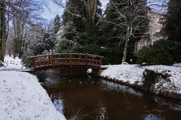 Rzeka Czerna Mała płynąca przez park dworski w mieście Iłowa w Polsce. Nad rzeką widać mosty i kładki dla pieszych. Jest zima, ziemię pokrywa śnieg. © boguslavus