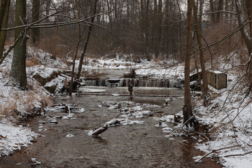 Wodospad na niewielkiej rzece płynącej przez las. Jest zima, rzeka w części jest zamarznięta, ziemia pokryta jest warstwą śniegu. © boguslavus