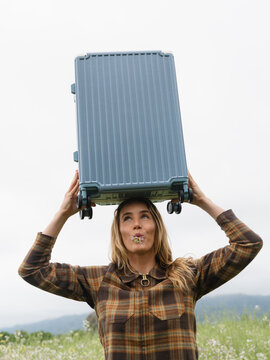 Woman Balancing Suitcase on Head in a Field During Cloudy Day
