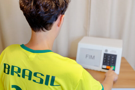 Homem brasileiro vestindo uma camiseta do Brasil votando em uma urna eletr&ocirc;nica. A tela exibe a palavra &ldquo;Fim&rdquo;, indicando que o voto foi conclu&iacute;do.