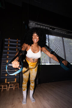 Young woman exercising with suspension trainer straps smiling at gym