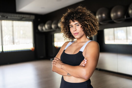 Confident transgender sportswoman posing with crossed arms in gym