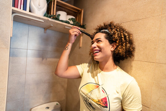 Young woman applying hair dye in bathroom and smiling