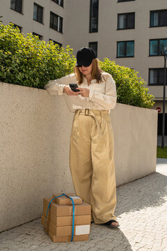 Young woman checking her phone while standing near a parcel
