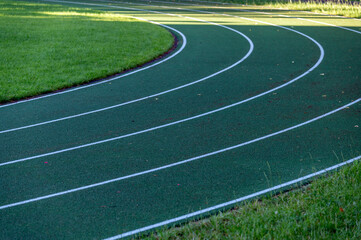 Empty Curved Running Track With Marked Lanes Beside Green Grass At Outdoor Athletic Field