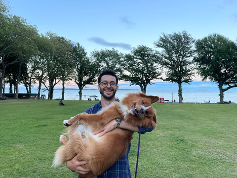 Man Holding a Happy Dog in a Scenic Park by the Water