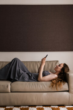 Woman Lounging on Sofa While Browsing Smartphone