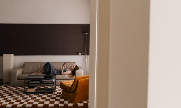 Woman Lounging on Sofa While Browsing Smartphone At Home