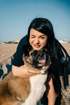 Woman Gently Hugs Akita Dog at Sunny Beach During Afternoon