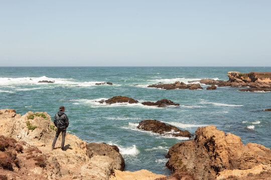 Man in Hoodie Standing on Beachside Cliff