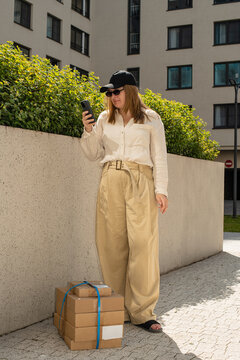 Young woman checking her phone while standing near a parcel