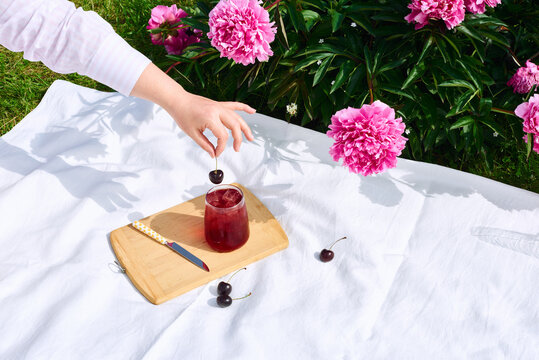 Refreshment with cherries under blooming peonies in sunlight