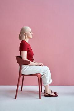 Portrait of a woman sitting against a pink background