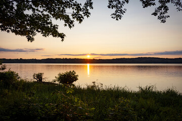 July sunset over a Western Kentucky lake, viewed through lush lakeside trees. Golden hour at Land Between the Lakes National Recreation Area.